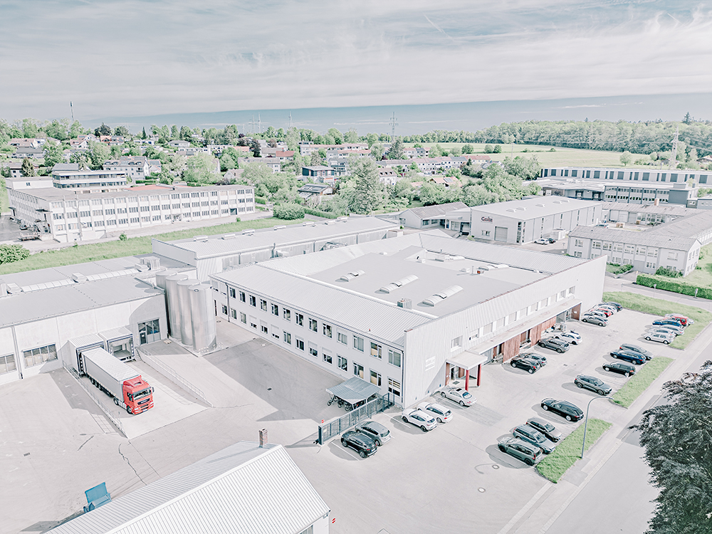 Aerial view of a large industrial building in a green, rural setting.