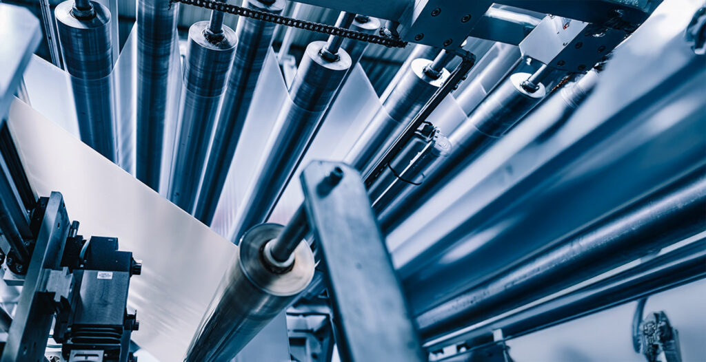 Close-up of a modern film extrusion machine in which several metal rollers process transparent plastic film.