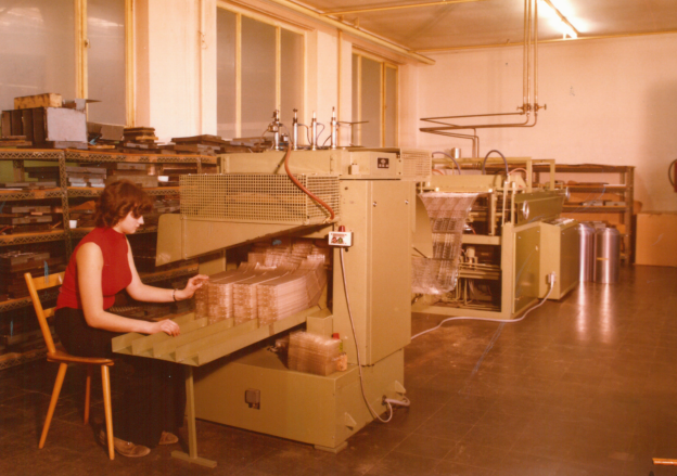 Retro photo of a production hall with several thermoforming machines. Several people in work clothes are operating the machines.